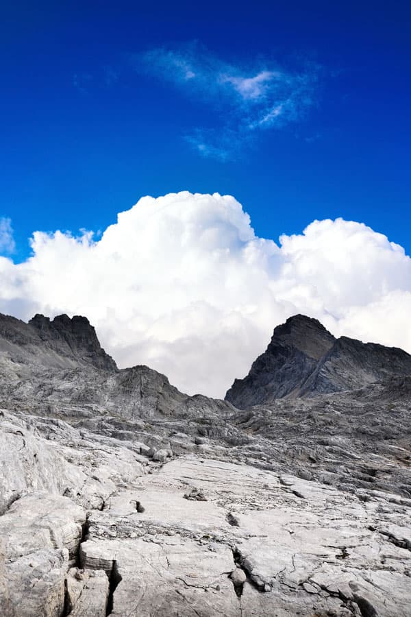 looking up a steep mountain into beautiful sky with a big cloud over mountain